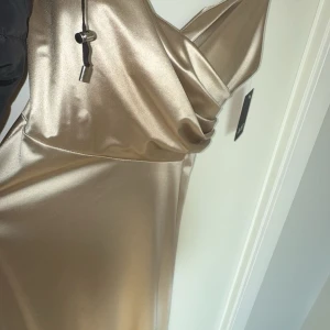 Champagnefärgad långklänning med snörning på ryggen - Säljer en glansig satin champagnefärgad långklänning med smala axelband och snygg snörning i ryggen. Klänningen har en elegant satinlook och figurnära passform, perfekt för bal eller speciella tillfällen. Helt oanvänd och bara testad i butik. Har köpt en annan så kommer ej ha användning av denna😊Orginalpris: 1200 Köpt för: 800. Klänningen är onesize så borde passa de flesta! Väldigt strechig.