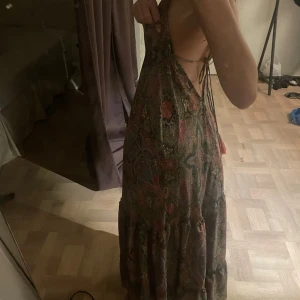 Mönstrad långklänning med volang och öppen rygg - Supersnygg långklänning med paisleymönster i grönt och rosa . Klänningen har volangdetaljer nertill, v-ringning och öppen rygg med smala knytband. Perfekt för sommarens alla tillfällen.