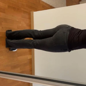 Svarta bootcut jeans med slits - Säljer ett par svarta jeans med bootcut passform och slits nertill vid bensluten. Jeansen har klassisk femficksdesign och är tillverkade i ett stretchigt jeanstyg som sitter snyggt över höfterna. 