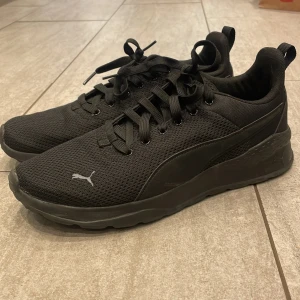 Svarta sneakers från Puma strl 42 - Säljer ett par svarta Puma sneakers i storlek 42. Skorna har en stilren design med mesh-ovandel, platt sula och rund tå. Puma-loggan syns på sidan och framtill. Perfekta för dig som gillar sportig och clean stil. Skorna har snörning och är tillverkade i syntetmaterial.