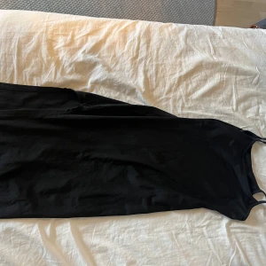 Svart långklänning från SHEIN - Svart långklänning från SHEIN med smala axelband och enkel, rak siluett. Klänningen är ärmlös och har en stilren look som passar perfekt för dig som gillar minimalistisk stil. Materialet är mjukt och lätt, vilket gör den skön att bära hela dagen.