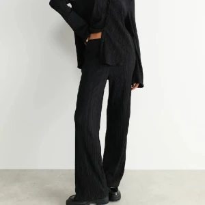 Svarta vida byxor med struktur - Plisserad medel låga byxa från Gina Tricot! Sjukt snygga men köpte tyvärr fel storlek så helt oanvända💕