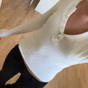 Vit ribbad långärmad tröja AWARE - Säljer en vit ribbad långärmad tröja från AWARE i storlek XS. Tröjan har v-ringning med fyra knappar framtill och sitter tight mot kroppen. 🤗
