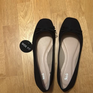 Svarta ballerinaskor med rosett - Svarta ballerinaskor från Shein med bred passform och fyrkantig tå. Skorna har en söt rosett framtill. Yttermaterialet är i syntet och sulan är platt för extra komfort. Perfekt för dig som vill ha stil och bekvämlighet i ett.