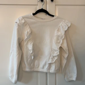 Vit tröja med volang - Supersöt vit tröja från Lindex med långa ärmar och breda spetsvolanger framtill och bak.Tröjan har rund hals och elastisk nederkant för skön passform🤍