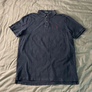 Mörkblå Piké från Polo Ralph Lauren - Säljer en mörkblå piké från Polo Ralph Lauren. Tröjan är i helt och fint skick, inga slitagemärken eller liknande men däremot möjligtvis lite urtvättad.  Storlek M.  Mått 📏📐 - Bröstvidd 51cm  - Bottenvidd 50cm - Plagglängd 64cm  Hör gärna av er vid frågor  ~ LoopSupply ~