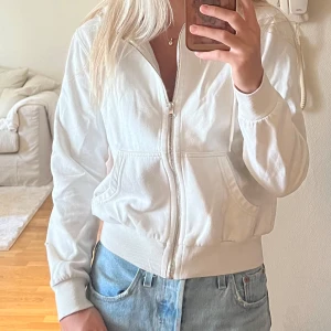 Vit hoodie med dragkedja från H&M  - Säljer en vit zip-up hoodie från H&M  i storlek XS.  Hoodien har dragkedja framtill, två fickor och huva med snörning. Mjuk bomullskänsla och ribbade muddar vid ärmslut och nederkant. 