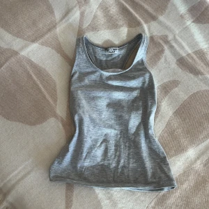 Ljusgrått linne från attitude - Säljer en enkel och stilren ljusgrått linne från attitude. Har en slim passform. Perfekt att matcha med jeans eller shorts för en chill look.