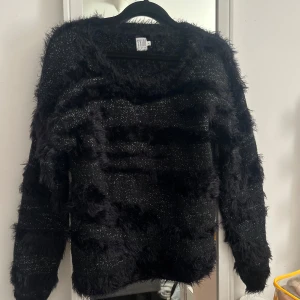 Glittrig svart tröja från Saint Tropez - Säljer en svart långärmad tröja från Saint Tropez i storlek M. Tröjan har glittriga inslag och fluffiga ränder som ger en cool textur. Perfekt för dig som gillar att sticka ut med en unik och trendig look. Mjuk och skön att bära, passar till många olika stilar.