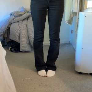 Svarta bootcut jeans med fickor - Snygga svarta jeans med bootcut passform och klassiska fickor bak med knappdetaljer. Jeansen har en mörk ton och sitter skönt över höfterna. 