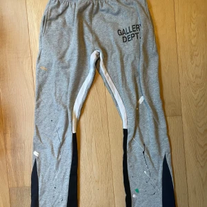 Gallery Dept. grå mjukisbyxor L - Grå mjukisbyxor från Gallery Dept. med svart tryck på ena benet och färgstänk som ger en kreativ vibe. Byxorna har svarta och vita paneler längs benen, elastisk midja och är tillverkade i mjukt bomullsmaterial. 