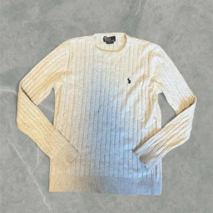 Grå kabelstickad tröja från Ralph Lauren - Snygg grå kabelstickad tröja från Polo Ralph Lauren med rund halsringning och broderad logga på bröstet. Den är  i storlek M och i superfint skick.