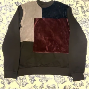 La Vichy färgblockad sweatshirt S - Säljer en unik sweatshirt från La Vichy i storlek S. Tröjan har coola färgblock i mörkblått, vinrött och beige på framsidan, med mjuka sammetspaneler. Resten av tröjan är svart med rund hals och långa ärmar. Perfekt för dig som gillar statement-plagg.