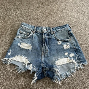 Blå jeansshorts med slitningar från Bershka - Säljer ett par blå jeansshorts från Bershka i storlek S. De har hög midja, fransiga kanter samt flera slitningar och hål både fram och bak. Köpte på vinted men dom passade inte så dom är i fint skick. 