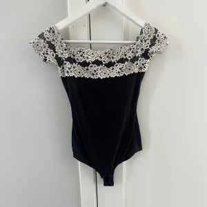  body från Intimissimi - Supersnygg svart body från Intimissimi med bred offshoulder spets upptill i vitt och svart. Tight passform och axelbandslös design som ger en elegant vibe.