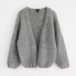 Grå stickad kofta  - Mysig grå stickad kofta från Lindex med loose passform och djup v-ringning. Koftan har långärmade ärmar och är perfekt att slänga på sig när det är kyligt ute. Enkel och stilren design som funkar till många olika outfits.