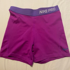 Nike Pro lila träningsshorts - Nike Pro shorts i en snygg lila färg med bred elastisk midja och diskret logga på benet. Tillverkade i Dri-FIT syntetmaterial som andas och håller dig torr under träningen. I storlek XL men dem är betydligt mindre i storleken, jag skulle säga att de passar storlek XS och S.