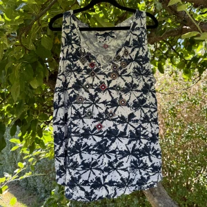 Odd Molly mönstrad linnetopp - Unik linnetopp från Odd Molly med coolt blått och vitt mönster. Toppen har v-ringning och är dekorerad med broderade detaljer och pärlor i olika färger framtill och baktill. Materialet är mjuk bomull och modellen är ärmlös, perfekt för varma dagar. Storlek 3 som enligt deras storleksguide motsvarar en storlek L.  Mer använd men fortfarande fint skick. 