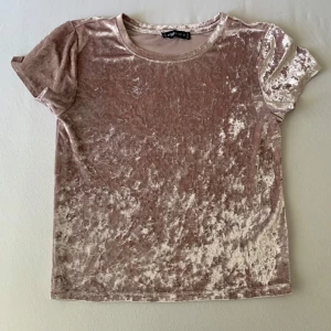 Rosa sammetst-shirt från FB Sister - Supermjuk t-shirt i krossad sammet från FB Sister i en ljusrosa ton. Klassisk rund halsringning och korta ärmar. T-shirten har en glansig finish som ger en lyxig känsla och passar perfekt till jeans eller kjol.