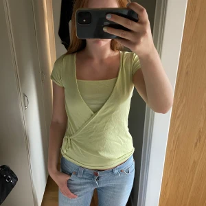 Ljusgrön omlottopp från H&M - Supersöt ljusgrön omlottopp från H&M med korta ärmar och knyt i sidan. Toppen har en smickrande v-ringning och är gjord i mjuk bomull, perfekt för en fräsch och somrig look. Enkel att matcha med jeans eller kjol för en chill stil.