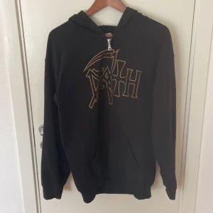 Death hoodie från Gildan, medium - Svart hoodie från Gildan med Death-logga och stort tryck från albumet 'The Sound of Perseverance' på ryggen. Tröjan har huva, dragkedja framtill och är tillverkad i en mjuk bomullsblandning. Perfekt för dig som gillar metal och vill sticka ut.