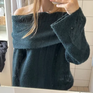 Mörkgrön offshoulder stickad tröja - INTE” STICKSIG” enligt en över sensorisk person. Supermysig stickad tröja i mörkgrönt med bred offshoulder-ringning och långa, vida ärmar. Perfekt för dig som gillar chill och oversized vibes. Materialet är mjukt och fluffigt, och tröjan har en loose passform som ger en avslappnad look.