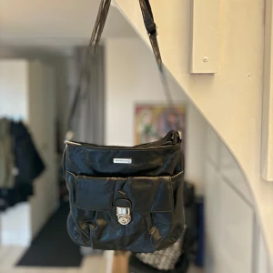 Svart axelväska från Daniel Ray - Daniel Ray svart axelväska i superskick. Väskan är i syntet och har en praktisk dragkedja på baksidan samt en ficka med  låsdetalj på framsidan. Mått ca 22x24cm utan axelrem.  Axelremmen är justerbar. Hämtas på Hägerstensåsen eller ök 🖤👜🖤