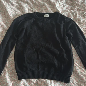 Svart stickad tröja från Vila - En enkel och stilren svart stickad tröja från Vila med rund hals och långa ärmar. Tröjan har ribbade muddar vid hals, ärmslut och nederkant. Perfekt för lager-på-lager och passar till jeans eller kjol.