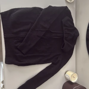 Svart hoodie i kashmir från Galeries Lafayette - Säljer en svart hoodie från Galeries Lafayette i 100% kashmir. Tröjan har dragkedja framtill, huva med snörning och långa ärmar. Perfekt för dig som vill ha en mjuk och lyxig hoodie med clean look och skön passform.