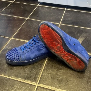 Blå Christian Louboutin sneakers med nitar - Säljer ett par blå sneakers från Christian Louboutin med coola nitar på tån och klassisk röd sula. Skorna är gjorda i mocka och har snörning framtill. Strl 42 passar 43. Lite små slitage på undersidan och samt en spik är av, har spiken i lådan om du så skulle vilja försöka lima tillbaka eller något liknande! (Tappat bort dusbagen) hör av er om ni undrar över något⚠️‼️pris ej hugget i sten!