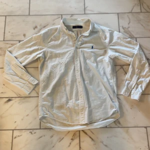 Vit skjorta från Ralph Lauren  - Vit klassisk skjorta från Ralph Lauren i 100% bomull. Plagget är i använt skick och den största defekten är kragen som förlorat lite av sin form men fungerar fortfarande. 