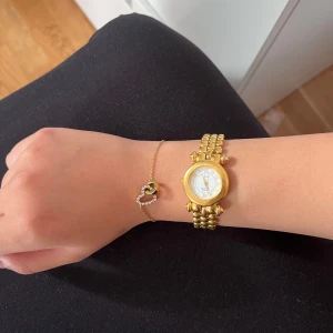 Guld vintage klocka med länkarmband - Säljer en snygg vintage guldig klocka från Anne Klein med rund urtavla och klassiskt länkarmband. Urtavlan är vit med romerska siffror och gulddetaljer. Klockan har en elegant och tidlös design som verkligen sticker ut på handleden. Köpte för 499kr på en marknad. 