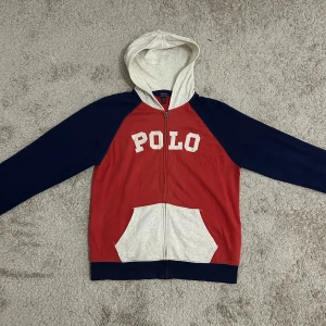 Polo Ralph Lauren Zip Hoodie Röd & Blå - Fin tröja från Polo Ralph Lauren. Köpt 2 år sedan, fast knappt använt. En liten fläck vid fickorna, inget farligt. Storlek ”170” men passar bättre för de som bär S. Skriv för mer info. Mindre pris för snabbaffär!