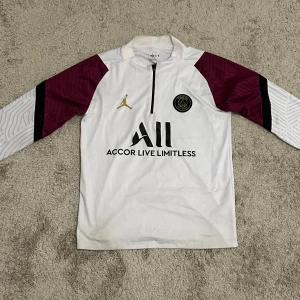 PSG x Jordan tracksuit vit - Snygg PSG långärmad fotbollströja i vitt med vinröda och svarta detaljer på ärmarna. Tröjan har halv dragkedja, guldigt Jordan-logga och PSG-emblem på bröstet. Nästan perfekt skick. Skriv för mer info, priset kan diskuteras vid snabbaffär!