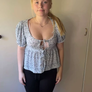 Blommig blus med knyt från Gina Tricot - Supersöt blommig blus från Gina Tricot i vitt och blått. Modellen har puffiga korta ärmar, knytning framtill och lätt v-ringning. Tunt och luftigt material, perfekt för varma dagar. Säljer då den inte kommer till användning längre!