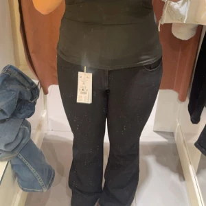 Svarta low waisted bootcut jeans från Gina tricot - Svarta Y2K jeans med bootcut-modell från Gina Tricot. Klassisk femficksdesign, silverfärgade knappar på bakfickorna och bälteshällor. Jeansen har en något utsvängd passform nertill och är tillverkade i ett stretchigt bomullsmaterial för skön känsla. 