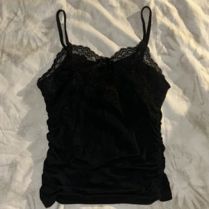 Svart spetslinne - Säljer en svart linnetopp med smala axelband och vacker spets upptill. Toppen har en liten rosett framtill, superskönt material❤️Säljer eftersom att den e för liten, använd bara 1 gång när den är testad. Pris kan diskuteras