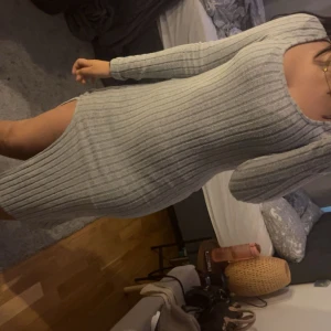 Grå ribbad stickad klänning med slits - Superfin grå stickad klänning med ribbat mönster och lång ärm. Klänningen är tight, har en snygg slits på sidan och rundad urringning. Perfekt för dig som gillar en enkel men ändå trendig look. 