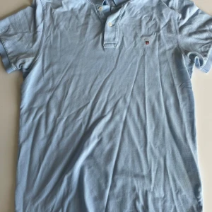 Ljusblå polo t-shirt från Gant - Snygg ljusblå pike från Gant med klassisk krage och två knappar vid halsen. Strl S