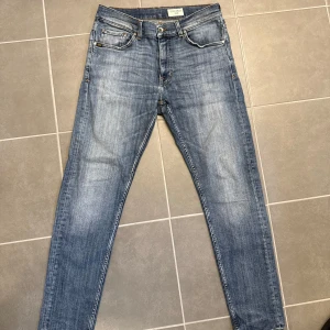 Tiger of Sweden blå jeans Evolve 32/30 - Snygga blå jeans från Tiger of Sweden i modellen Evolve. De har klassisk femficksdesign, smal passform och raka ben. Jeansen är tillverkade i Italien och har coola slitningar och kontrastsömmar. Perfekta för dig som gillar stilrena och moderna jeans.