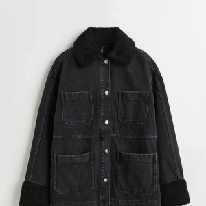 Svart jeansjacka med teddykrage - Säljer en svart jeansjacka från H&M med mjuk teddykrage och teddyfoder vid ärmsluten. Jackan har fyra stora fickor framtill och silverfärgade knappar. Passformen är loose och jackan har en cool, oversized vibe som funkar till jeans och sneakers.