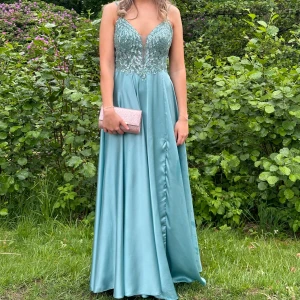 Balklänning - Jag säljer min vackra turkosa balklänning med glittriga paljetter och handbroderade detaljer. Klänningen har v-ringad urringning, tunna axelband och ett flowigt satintyg som faller fint. Klänningen är använd endast en gång och har efter användning tvättats professionellt hos Johans högtidskläder (värde 500kr), så den är i nyskick. Inköpt helt ny på Johans högtidskläder i Göteborg för 7000kr. Jag är 170cm lång och klänningen sitter perfekt med ett par låga klackar. Klänningen är i storlek 36.