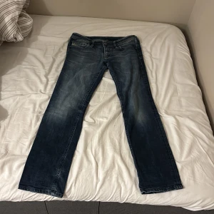 Diesel jeans i mörkblå straight fit - Snygga mörkblå jeans från Diesel med klassisk femficksdesign och coola slitningar. Modellen har raka ben och normal passform, med Diesel Industry-logga på myntfickan och detaljerade bakfickor. Perfekta för dig som gillar street och casual stil.