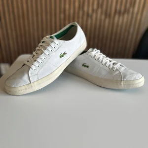Vita sneakers från Lacoste Sport - Snygga vita sneakers från Lacoste Sport med klassisk grön krokodil-logga på sidan. Skorna har snörning, rund tå och grön sula undertill. Ovandelen är i skinn och insidan har gröna detaljer. Perfekta för dig som gillar stilrena och sportiga skor.Lite tecken på slitage men annars i bra skick.