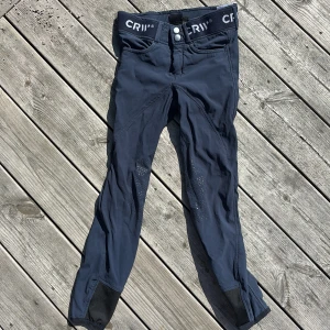Mörkblå ridbyxor från CRW, stl 140 - För barn. Snygga mörkblå ridbyxor från CRW med elastisk midja och dubbla knappar framtill. Byxorna har silikonprint på insidan av benen för extra grepp. 