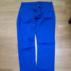 Blå byxor från KappAhl, storlek 170 - Snygga blå byxor från KappAhl i storlek 170. Byxorna har klassisk femficksdesign och raka ben. Tillverkade i ett mjukt bomullsmaterial med lite stretch för extra komfort. Perfekta för dig som vill ha en färgklick i garderoben.