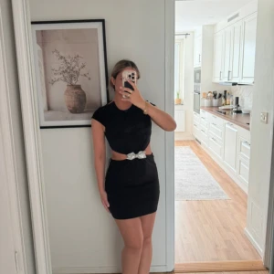 Svart kort klänning med cut-out och rosett - Snygg svart kort klänning med cut-out i midjan och en glittrig rosett framtill. Klänningen har korta ärmar och figurnära passform, perfekt för dig som vill sticka ut. Storlek M men känns som S 