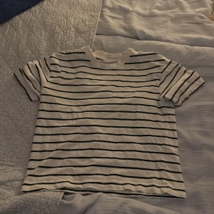 Vit och svart randig t-shirt - Snygg vit t-shirt med svarta horisontella ränder och klassisk rund hals. Modellen är kortärmad och har en relaxed passform som funkar till jeans eller shorts. Perfekt för dig som gillar enkel och stilren design.