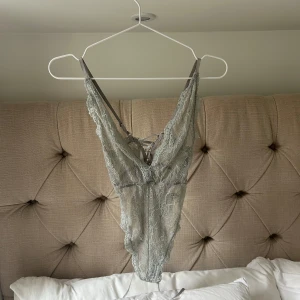 Ljusgrå/blå spetsbody med snörning - Superfin ljusgrå/blå body  i spets med v-ringad front och snygg snörning i ryggen. Tunn spets med blommigt mönster och smala axelband. 