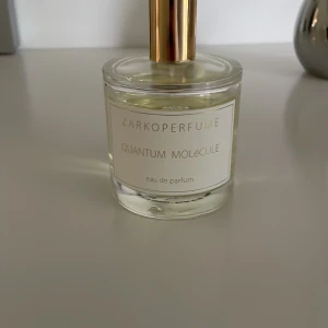 Zarkoperfume Quantum Molécule 100ml - Quantum Molécule från Zarkoperfume är en exklusiv eau de parfum i en stilren, rund glasflaska med guldigt sprayhuvud. Flaskan rymmer 100 ml och har en transparent, ljusgul vätska. Minimalistisk etikett i vitt och guld ger en lyxig känsla.